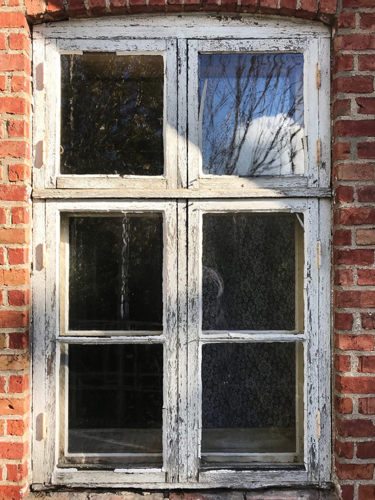 Tegelfasad och gamla flagnande fönster med handblåst glas.