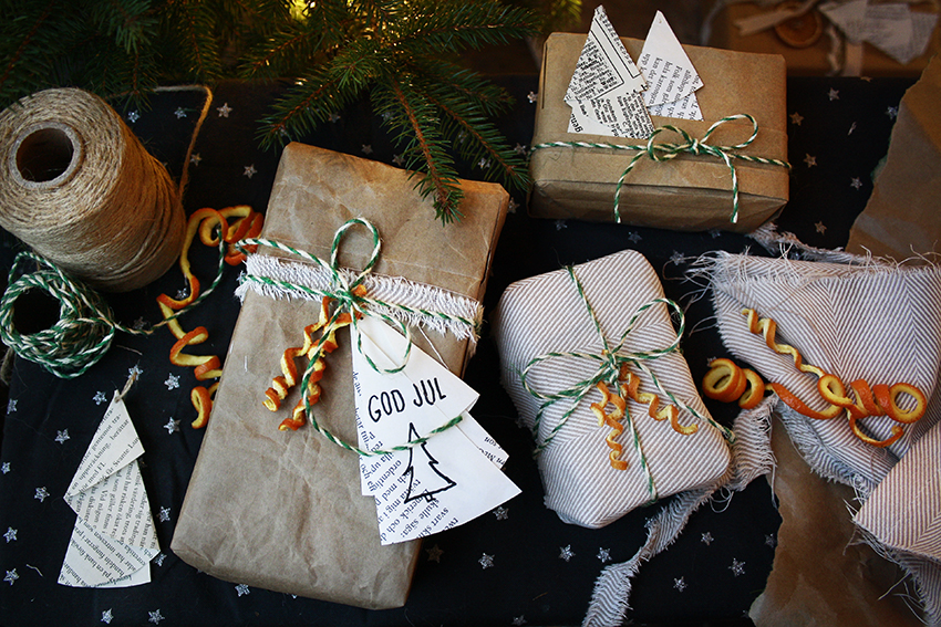 Fint inslagna paket av återbrukat papper och tygbitar ligger under julgranen. 